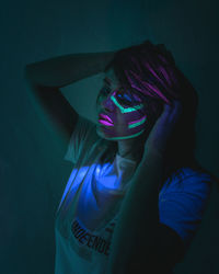 Woman with neon face paint against black background