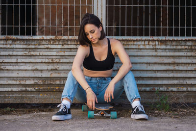 Full length of young woman sitting on skateboard outdoors