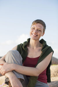 Portrait of happy woman relaxing on rock against clear sky