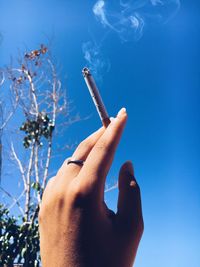 Cropped hand smoking cigarette against clear blue sky