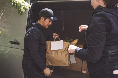 Delivery man talking to female colleague while holding package near truck