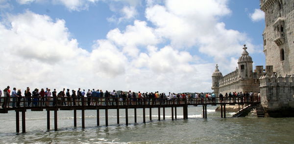 Group of people on wooden pedestrian bridge in front of stone tower