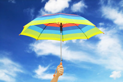 Cropped hand holding colorful umbrella against blue sky