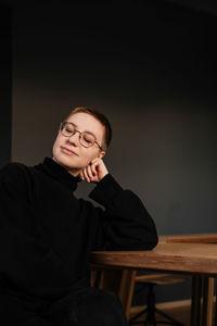 Smiling young woman with short hair in eyeglasses and black sweater sitting at the table in office