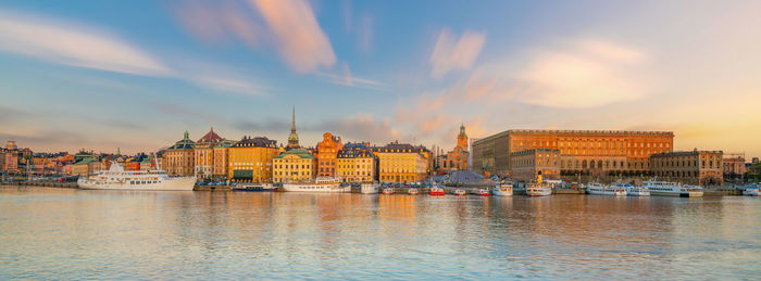 Buildings by river against sky during sunset