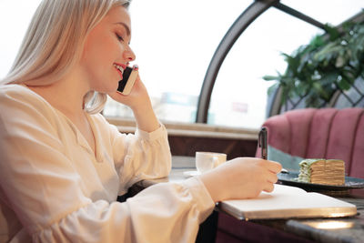 Side view of young woman using phone while sitting on table