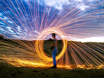 Side view of man spinning wire wool against cloudy sky