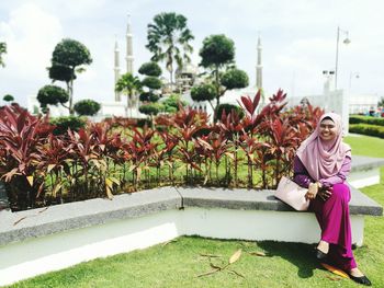 Smiling woman in hijab sitting on retaining wall at islamic heritage park