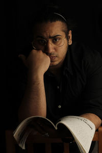 Portrait of young man with book against black background
