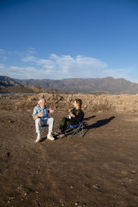 Woman and her grandfather talking while sitting on camping chairs outdoors in nature.