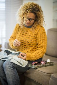 Young woman sewing on sofa