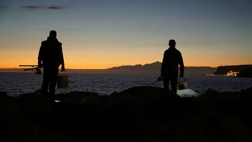 Silhouette of fishermen standing by sea against sky during sunset