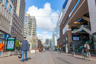 People walking on street amidst buildings in city against sky