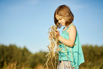 Cute little girl sits on mown rye in the field in summer