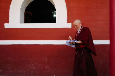 Side view of man standing against red wall