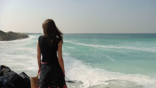 Rear view of woman standing at beach against sky