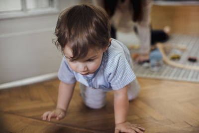 Cute baby boy crawling on harwood floor with mother in background