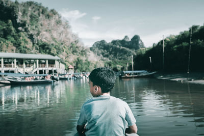 Rear view of boy sitting in boat on lake