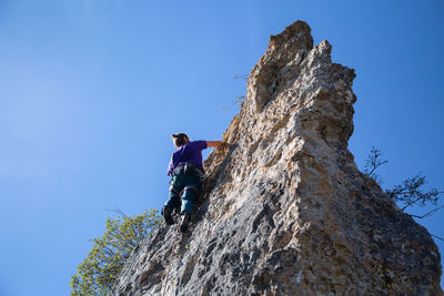 Low angle view of man climbing rock against sky