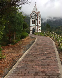 Footpath amidst trees and building against sky