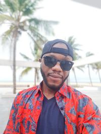 Portrait of young man wearing sunglasses standing against trees