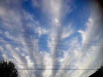 Low angle view of electricity pylon against cloudy sky