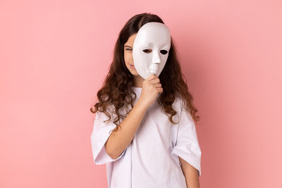 Portrait of woman wearing mask against pink background