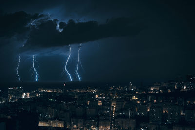 Illuminated cityscape against sky at night during a storm