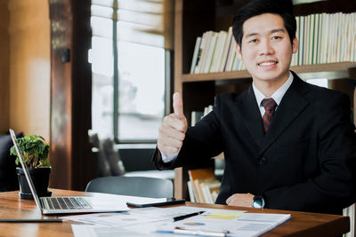 Portrait of confident businessman gesturing thumbs up in office