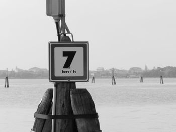 Information sign on wooden post by sea against sky