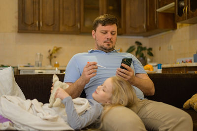 Dad calls mom, doctor via video to advise on the childs treatment, thermometer. telemedicine.