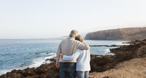 Rear view of couple standing on land by sea against sky