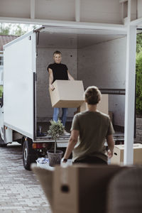 Female looking at friend while carrying cardboard box during relocation