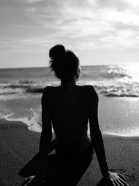 Woman sitting on beach against sky