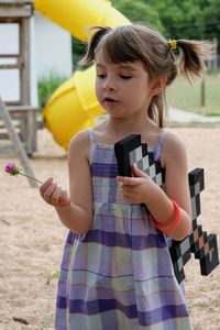 Close-up of girl holding toy sword while looking at flower in playground