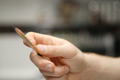 Cropped hand of man holding pencil in kitchen