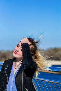 Smiling woman with hand in hair against sky