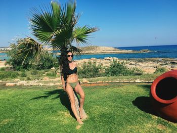 Portrait of young woman on palm tree by sea against clear sky