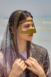 Close-up of young woman wearing traditional clothing standing at beach against sky