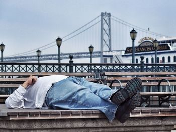 Low section of man with bridge against sky in city