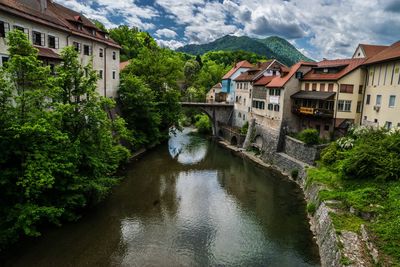 Arch bridge over river amidst buildings against cloudy sky