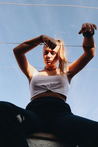 Low angle view of young woman sitting against sky