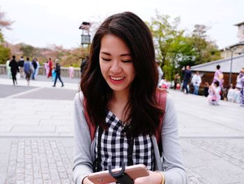 Smiling young woman using mobile phone in city