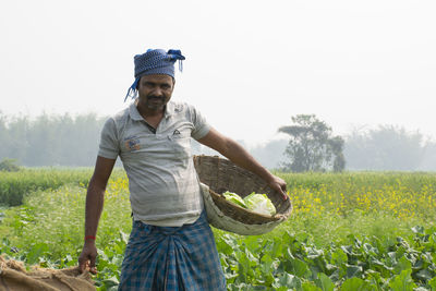 Full length of young farmer standing on field with vegetable basket