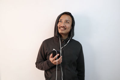 Portrait of smiling young man holding camera while standing against white background