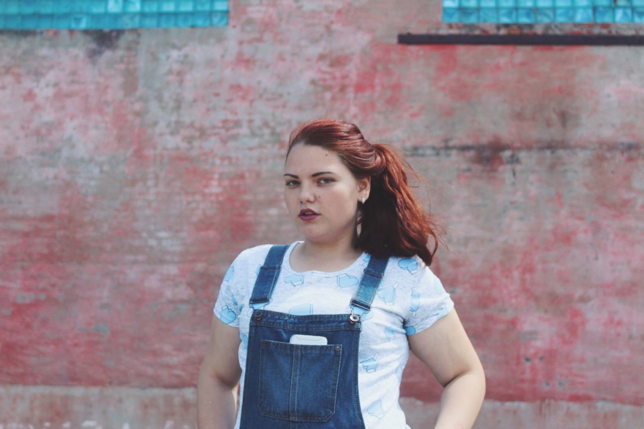 BEAUTIFUL YOUNG WOMAN STANDING AGAINST WALL