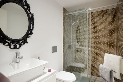 Interior of a modern bathroom decorated a black mirror frame with brown tiles with a shower cabin