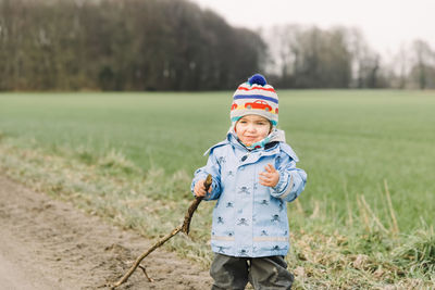 Cute boy holding tree stick standing on field