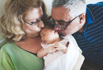 Close-up of grandparents kissing granddaughter at home