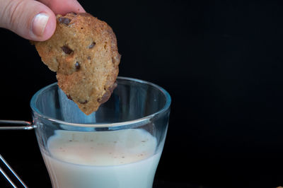 Close-up of hand holding chocolate cookie over a glass of milk